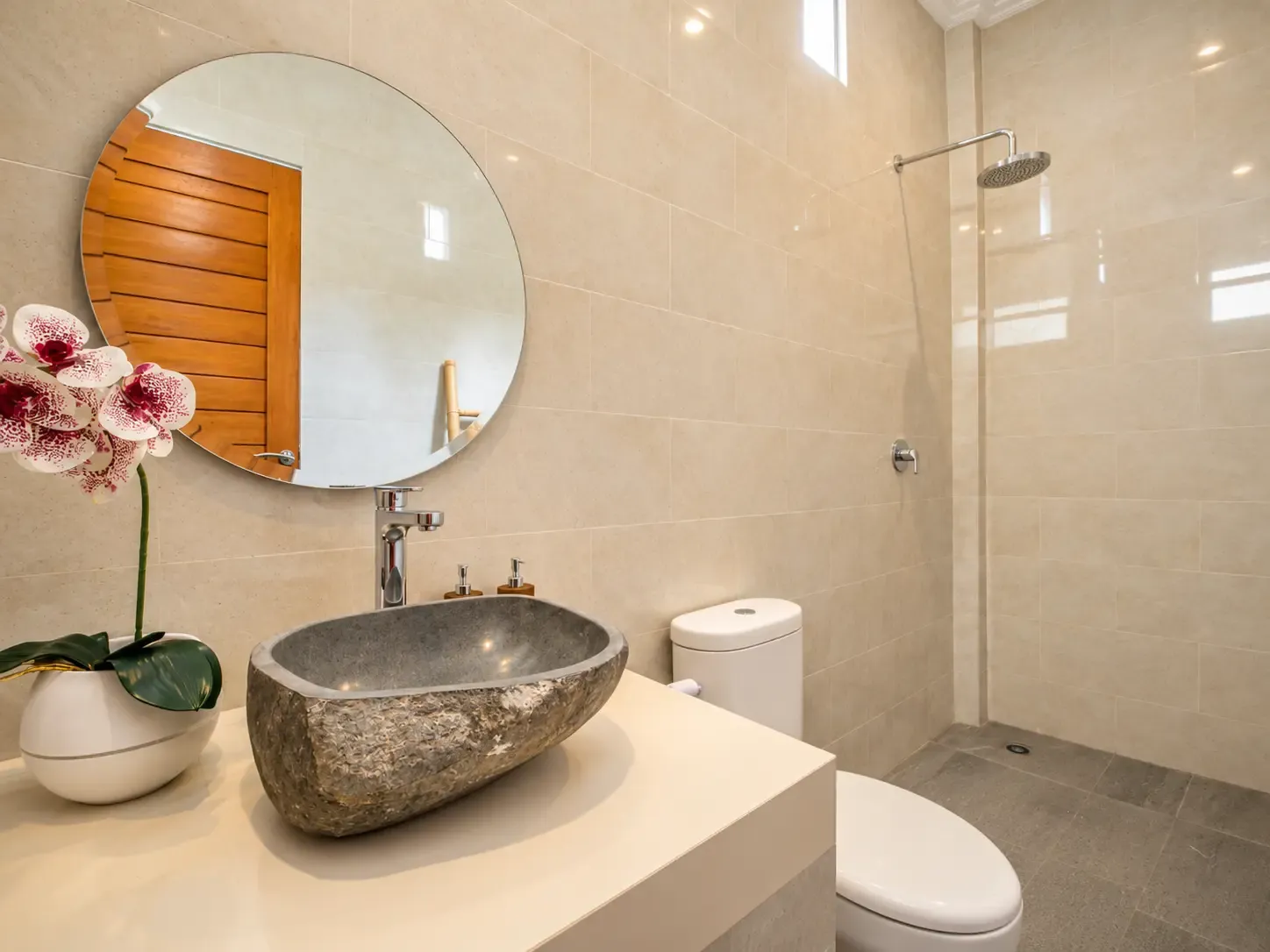 Baño Cahyana House con lavabo de piedra de río y espejo redondo.