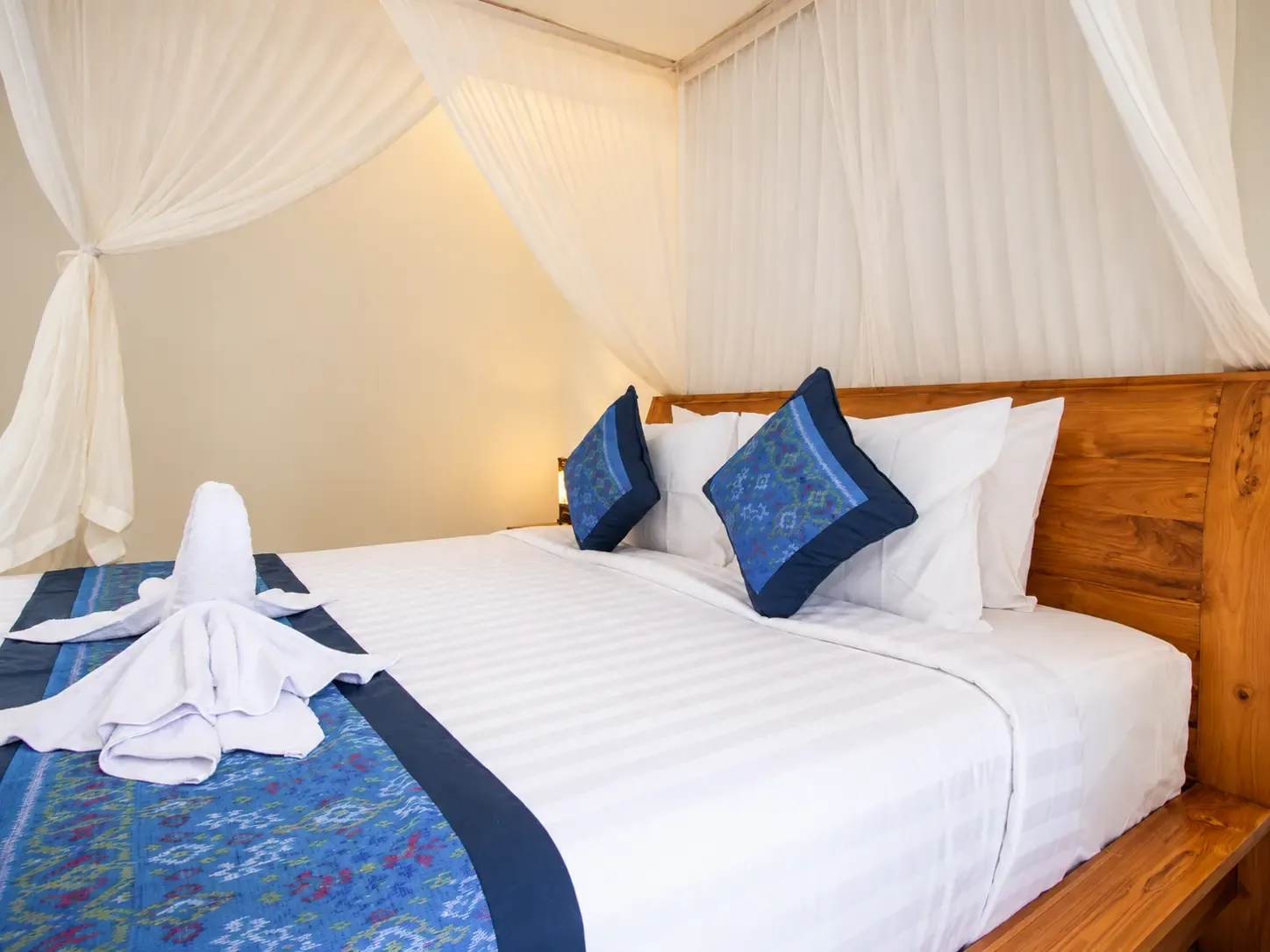 Cama Cahyana House con un cisne de toalla y cojines azules.